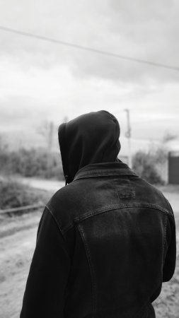 Черно-белая фотография мужчины в толстовке с капюшоном, идущего по грунтовой дороге.